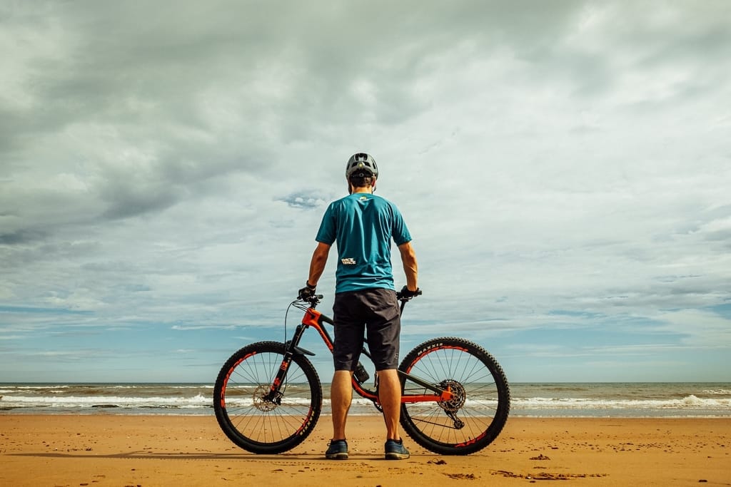 Man standing on the beach with his bike