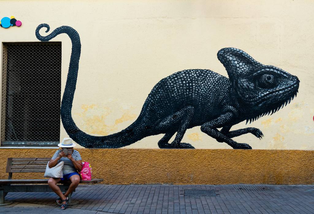 Giant painted mural of a chameleon with a person sitting underneath.