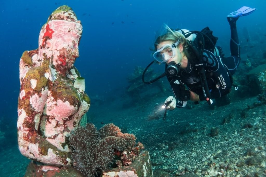 Girl scuba diving with underwater statues