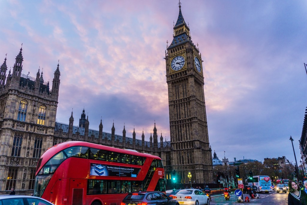 Red bus driving in front of Big Ben in London, UK